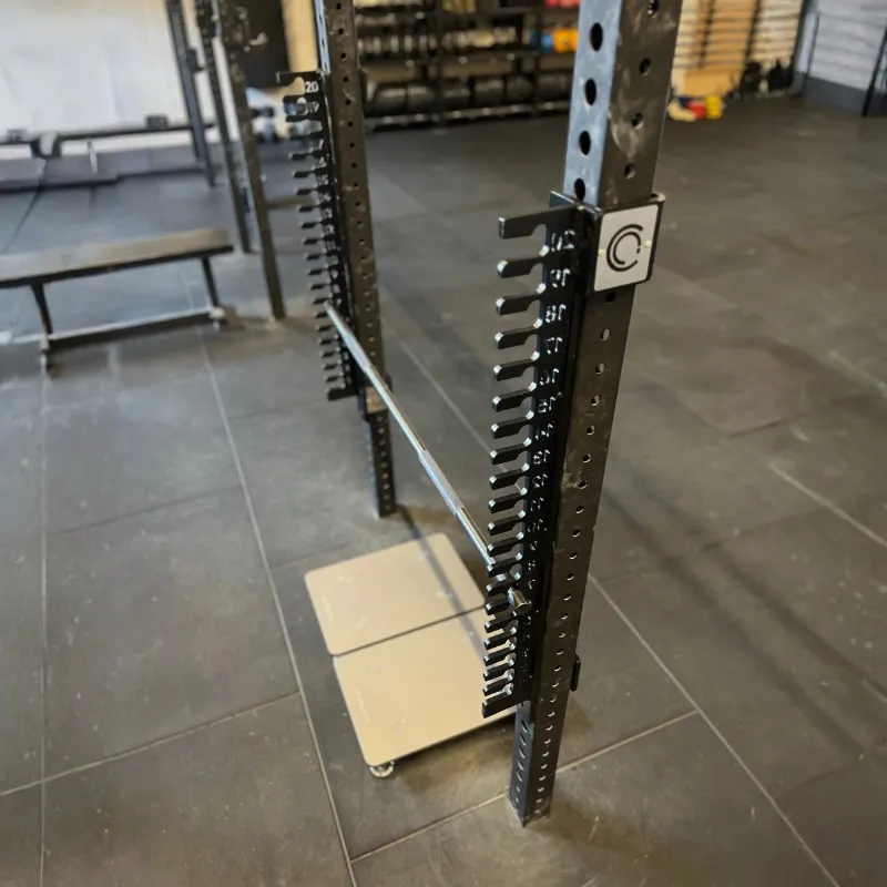 IMTP Extension mounted in a squat rack in a gym, pull bar set low in the notched uprights above a pair of force plates on the floor